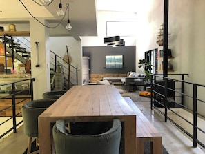 Ein zeitgemäßer Wohnraum mit einem Holztisch, einer Treppe, einer Couch und einem Bücherregal.
