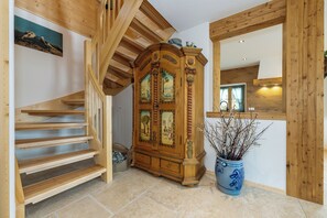 Eine Holztreppe, ein großer, verschnörkeltes Schranks und eine Vase mit Zweigen.