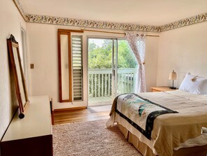 Une chambre à coucher comprenant un lit, une table de chevet, une lampe, une fenêtre avec des volets, une porte et un balcon avec une balustrade.
