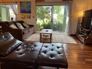 Un salon avec un canapé en cuir marron, une table basse en bois et un meuble pour la télévision, sur lequel est posé un téléviseur à écran plat.