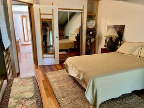 Une chambre à coucher avec un lit, un miroir, un ventilateur et une porte donnant sur une autre pièce.