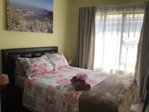 Un dormitorio con cama, mesita de noche, lámpara, un cuadro y ventana con cortinas.