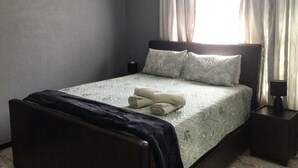 A bedroom with a bed, a nightstand, a lamp, a painting, and curtains.
