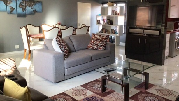 A modern living room with a grey sofa, a glass coffee table, and a patterned rug.