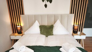 A neatly made bed with a green blanket, white pillows, and two bedside tables with lamps. - Apartment with balcony for max. 4 persons (Prien am Chiemsee)