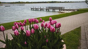 A waterfront view with a paved walkway, a wooden dock, and a row of pink tulips in a large planter. - Apartment with balcony for max. 4 persons (Prien am Chiemsee)