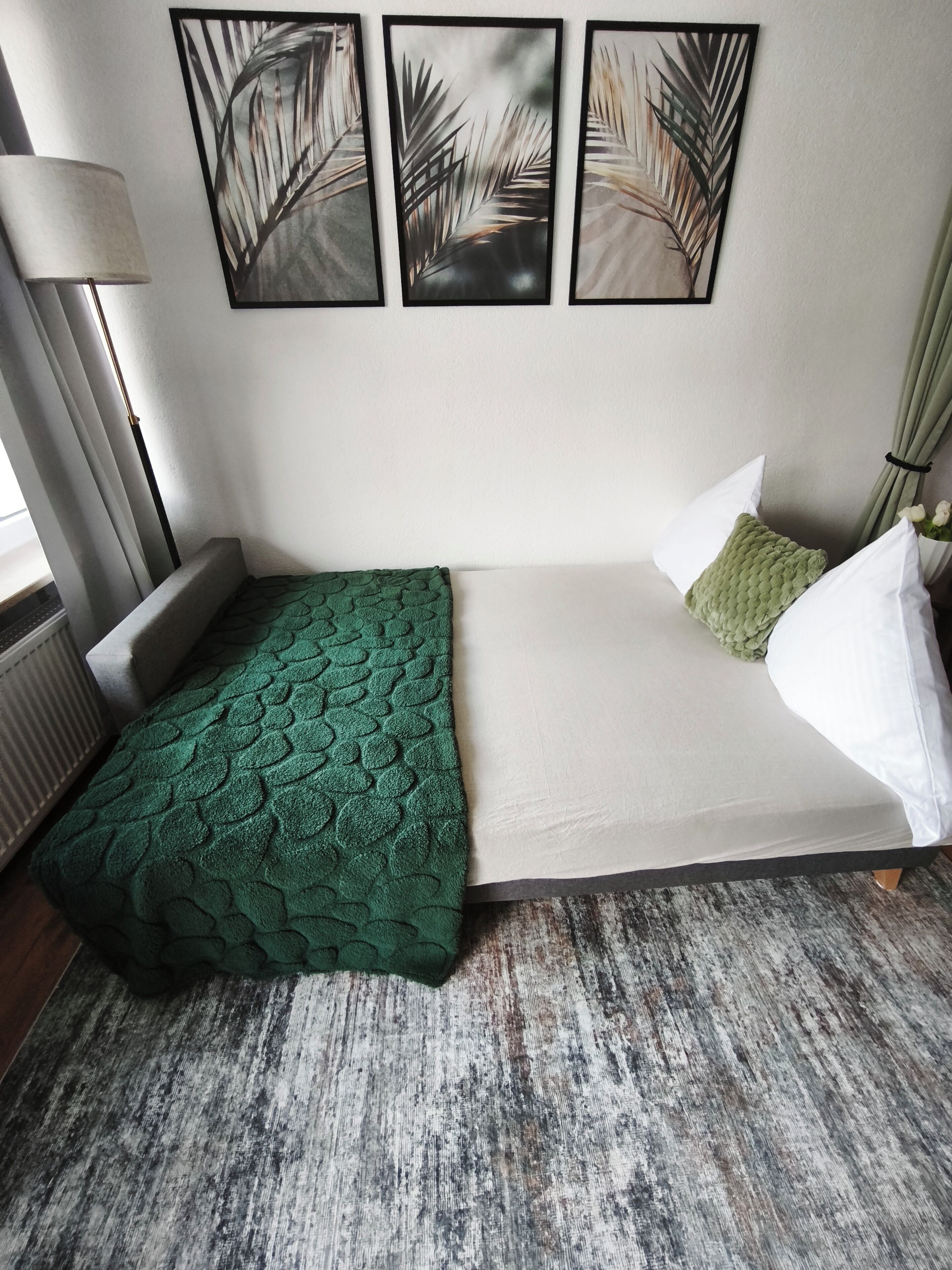 Ein Einzelbett mit einer grün gemusterten Decke, weißen Kissen und einem grauen Teppich.