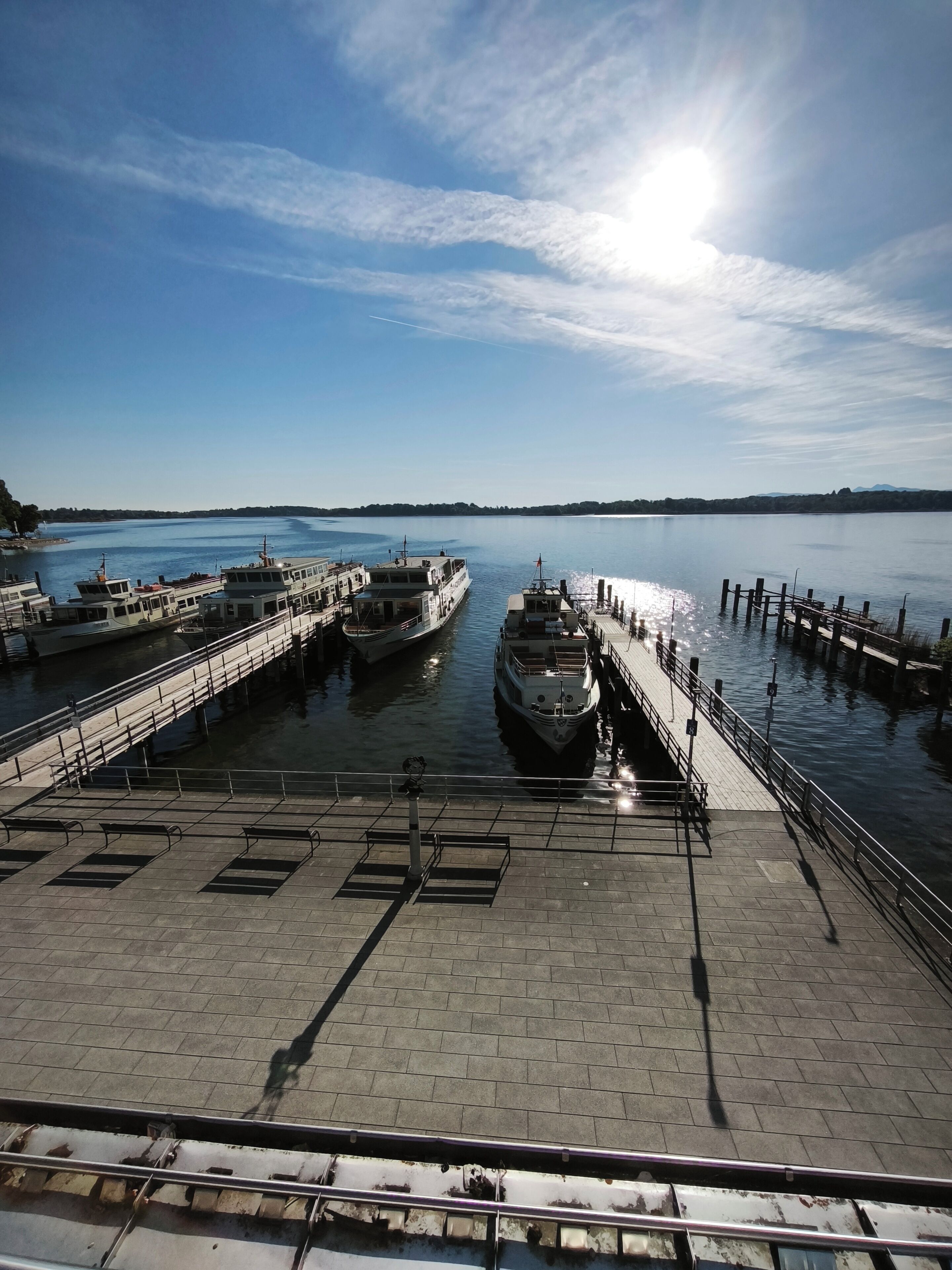 Ein Steg am Wasser mit vertäuten Booten, ein klarer Himmel und ruhige Wasserfläche.