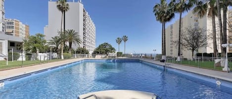 Una piscina con agua azul cristalina, rodeada de palmeras y edificios.