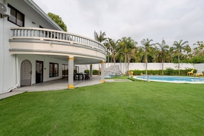 Ein zweistöckiges Haus mit überdachter Terrasse, Swimmingpool und gepflegtem Rasen.