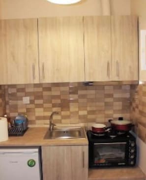 Una cucina con pensili e basi in legno, zoccolo in piastrelle, lavello, forno a microonde e un piccolo frigorifero.