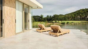 Un bâtiment moderne à la façade vitrée, doté de deux fauteuils de jardin en bois et offrant une vue sur un lac et la verdure environnante.