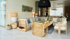 Un salon moderne avec un canapé, une table à manger et des chaises. Un grand miroir orne le mur, et un luminaire suspendu éclaire la pièce.