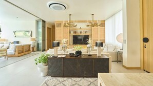 Un salon moderne avec un îlot central, un ensemble de canapés, un téléviseur et un luminaire décoratif au plafond.