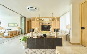 Ein modernes Wohnzimmer mit einer zentralen Kücheninsel, einer Sofagarnitur, einem Fernseher und einer dekorativen Deckenleuchte.