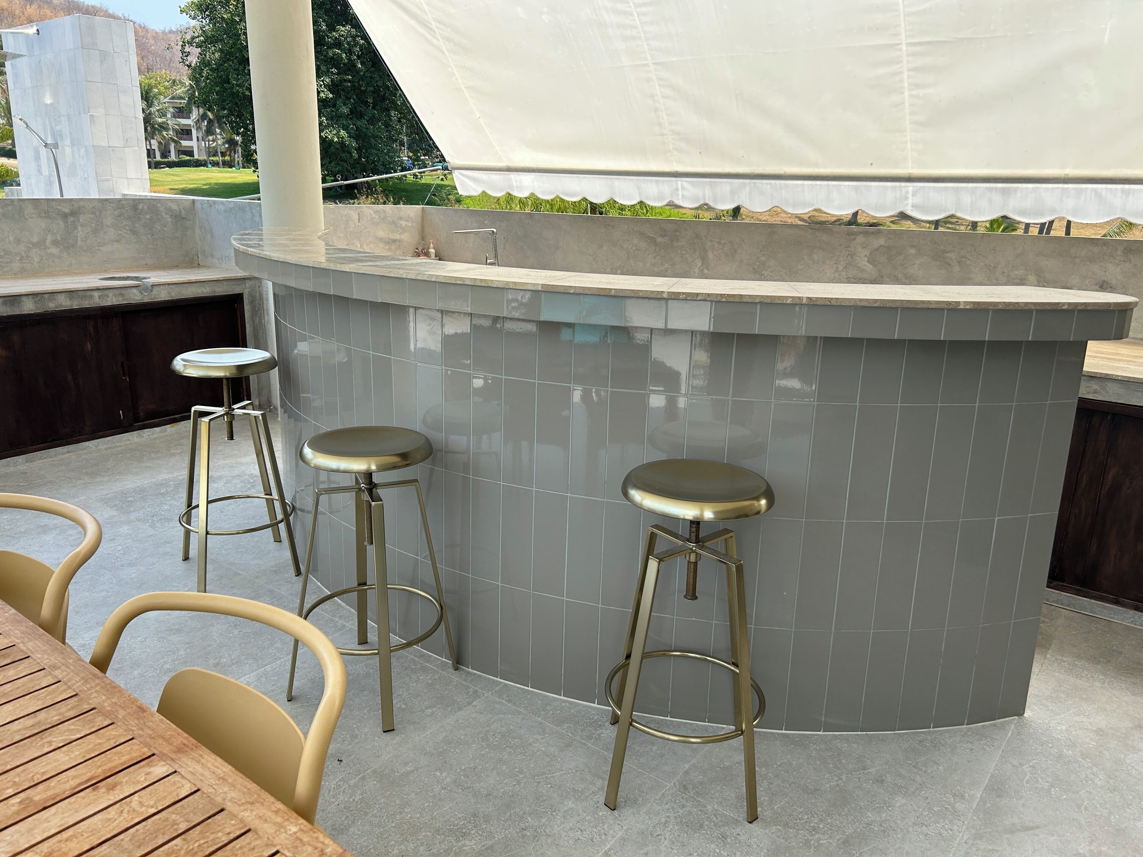 An outdoor bar area with a tiled counter, two stools, and a wooden table.