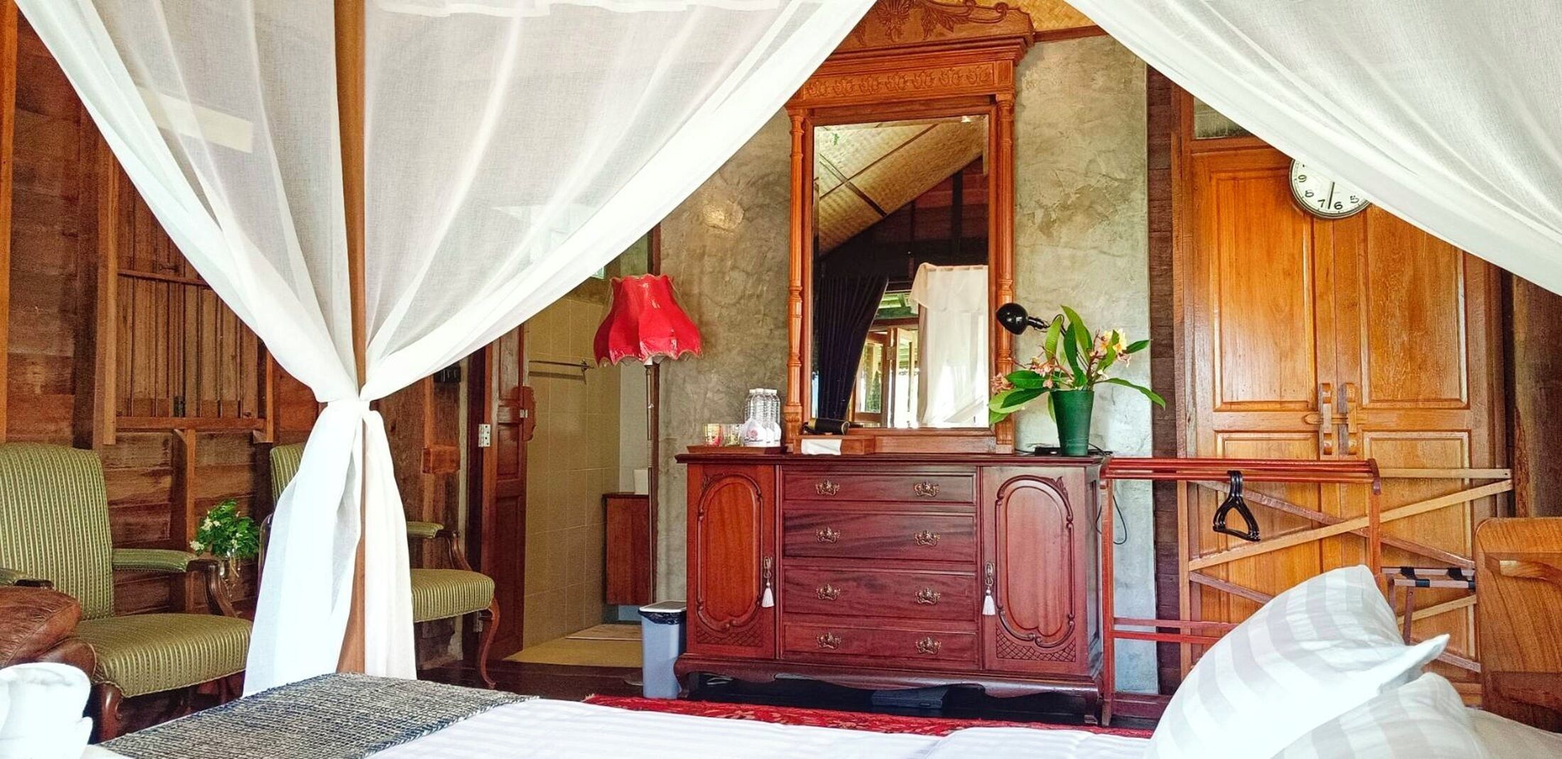 A bedroom with a canopy bed, wooden furniture, a mirror, and a red lamp.