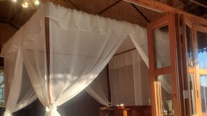 Habitación con cama bajo un dosel, suelo de madera y puerta de madera con paneles de vidrio.