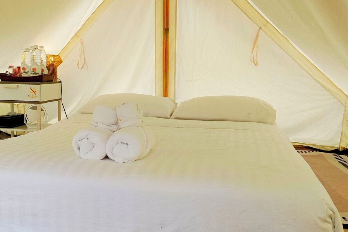 Una camera a tenda con un letto, cuscini, un comodino con bottiglie e una lampada.