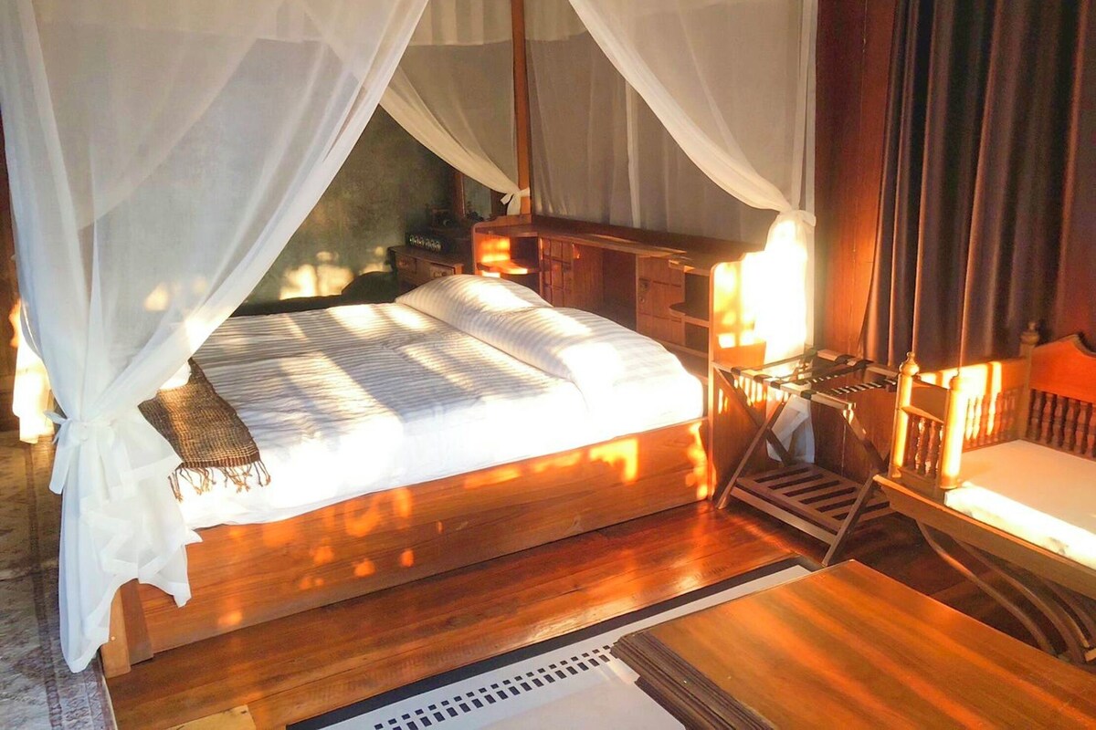 Un letto a baldacchino, una testiera in legno, un comodino e un tavolino di servizio.