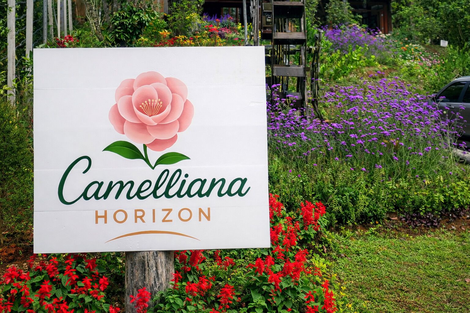 A sign for Camelliana Horizon with a rose graphic, surrounded by lush greenery and flowers.