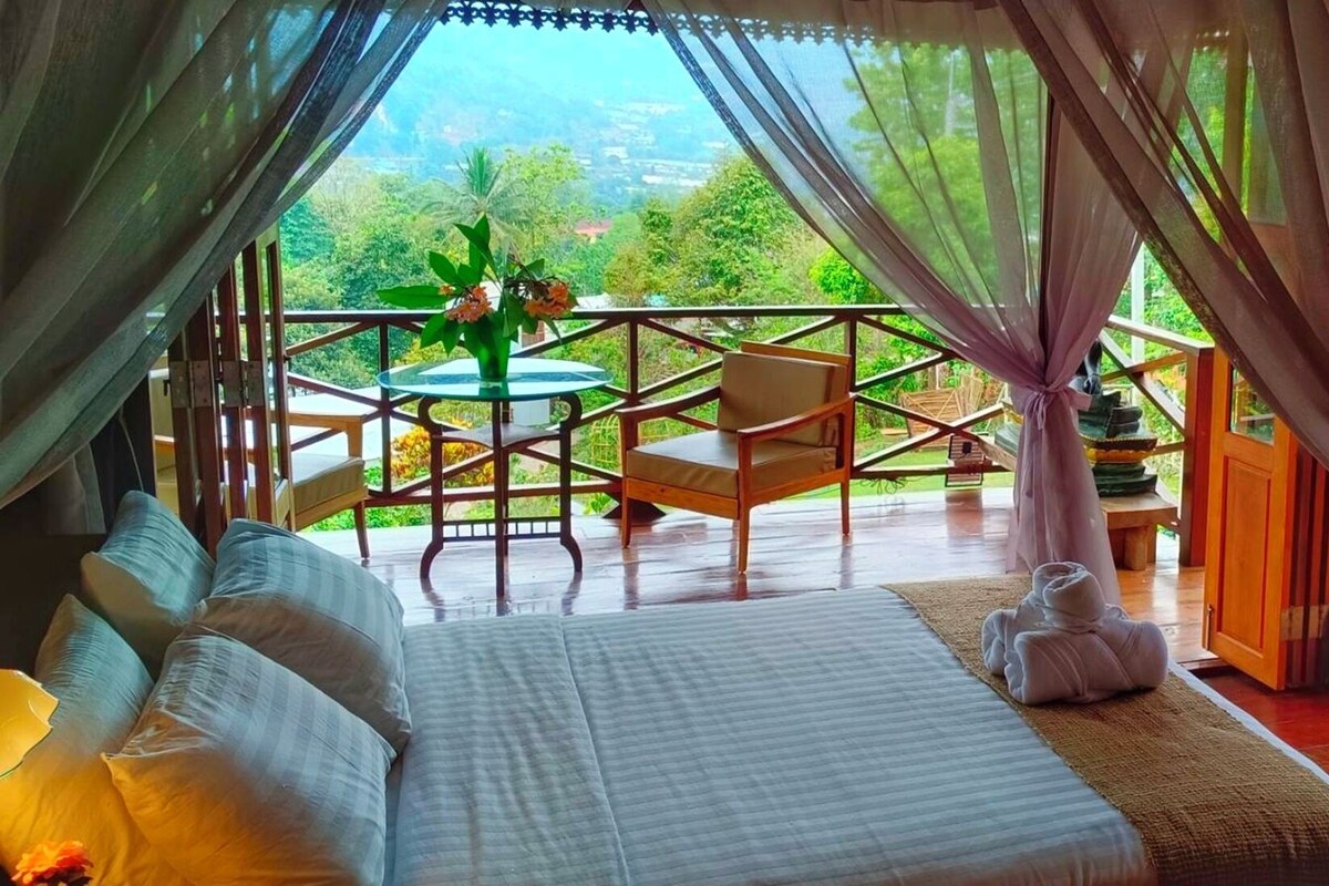 Una camera da letto con un letto, un tavolino e sedie, e vista sul verde circostante.