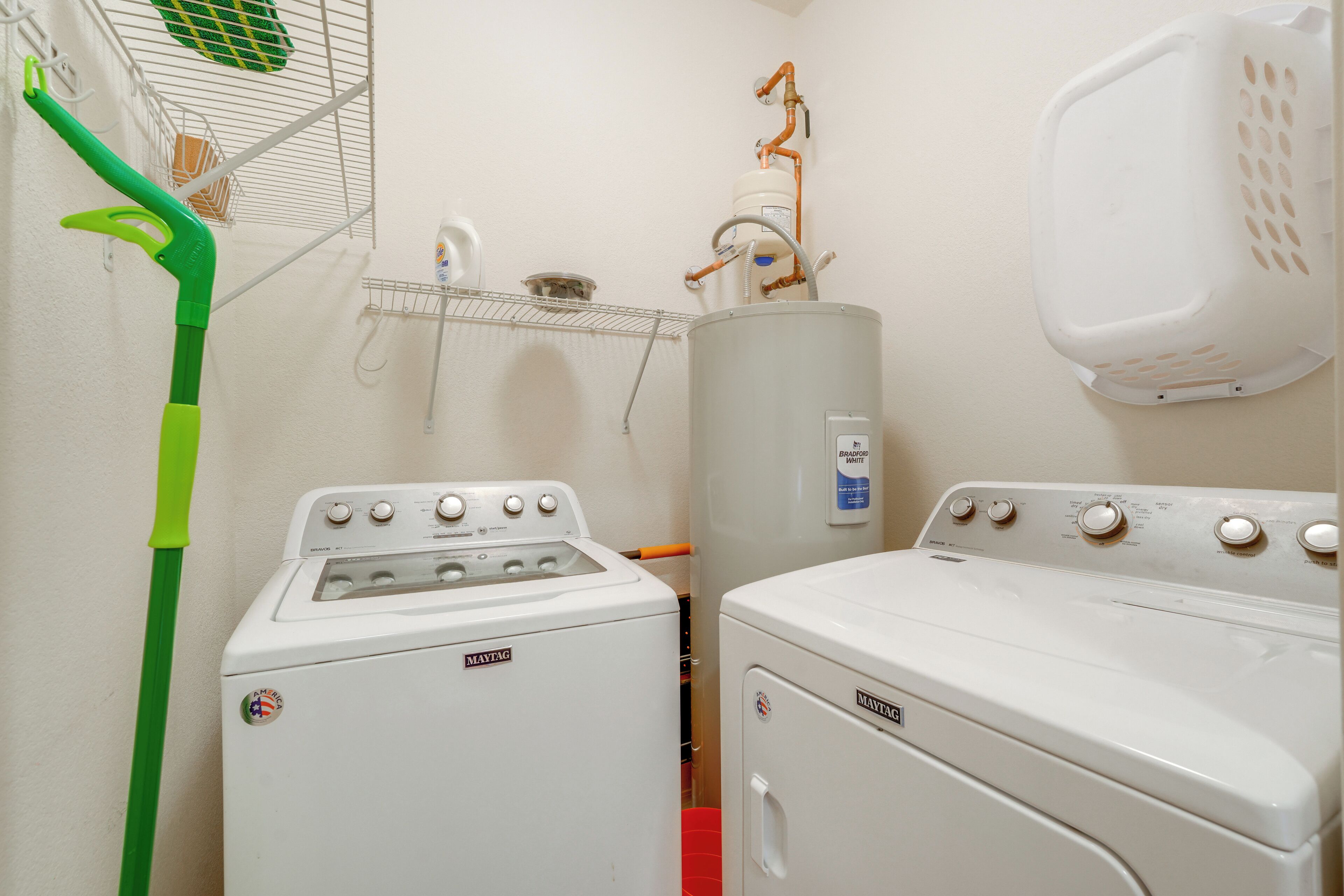 Zona de bugaderia amb dues rentadores i assecadores Maytag, una fregona verda, un tendal metàl·lic i una paret blanca.