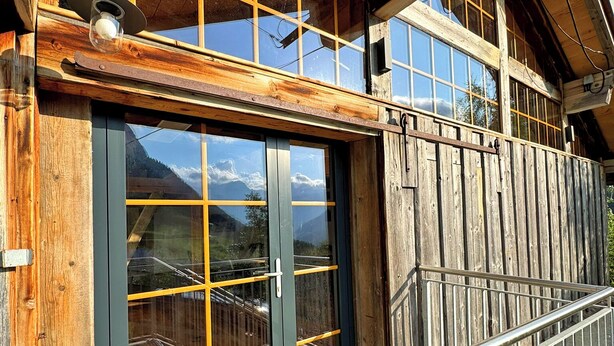A wooden building with a metal staircase and a glass door leading to a balcony.