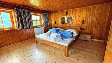 Una habitación con paneles de madera, una cama, una ventana con cortinas, un radiador y una mesita de noche pequeña.