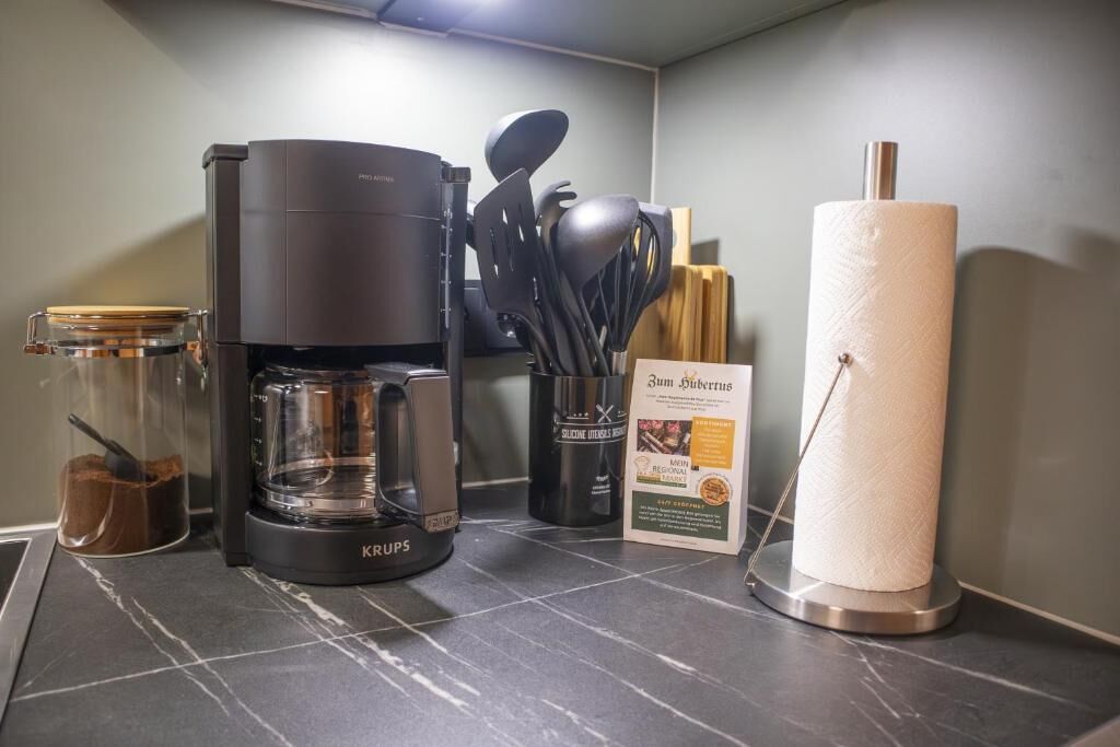 A coffee maker, a paper towel holder, a spice rack, and a glass jar on a kitchen counter.