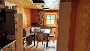 A wooden cabin interior with a kitchen, dining area, and a window with a view.