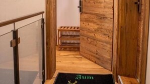 A wooden interior hallway with a glass railing, a wooden door, and a doormat with 'Zum Libertus' text.