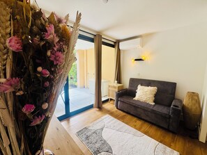 A living room with a sofa, a decorative vase with dried flowers, a rug, and a sliding glass door leading to an outdoor area. - Superb renovated T2 - air conditioning - terrace - swimming pool - tennis court (Cannes)