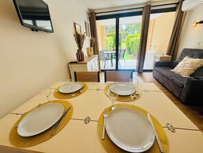 A dining area with a table set for four, a sofa, and a view of the garden through the glass doors. - Superb renovated T2 - air conditioning - terrace - swimming pool - tennis court (Cannes)
