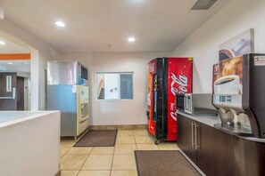 Una zona de cocina con refrigerador, microondas, máquina de Coca-Cola y cafetera.