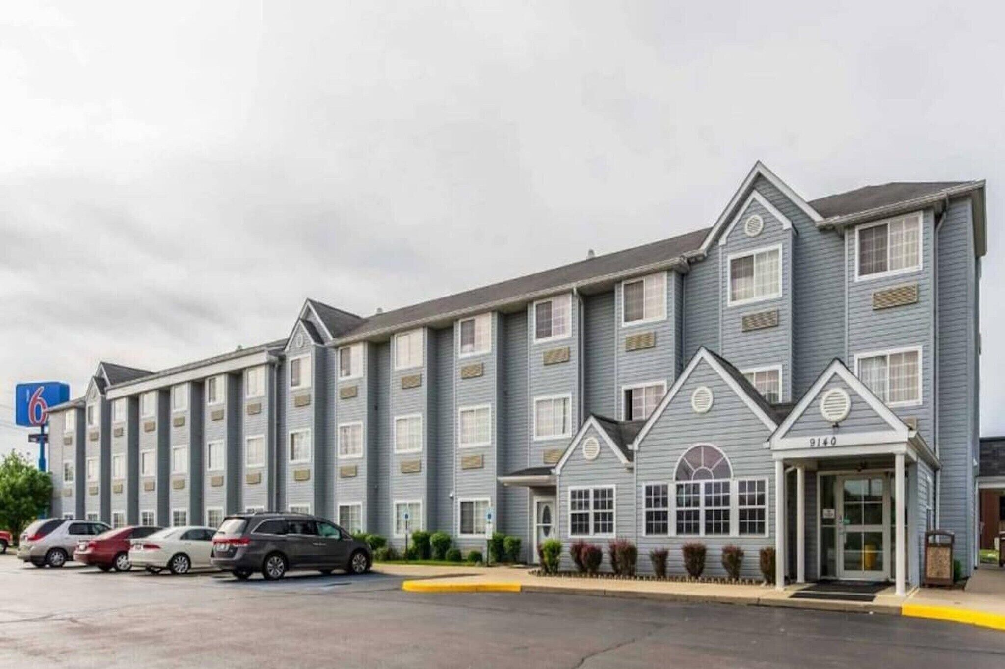 A multi-story hotel with a central entrance, parking lot, and a sign indicating the number of rooms.