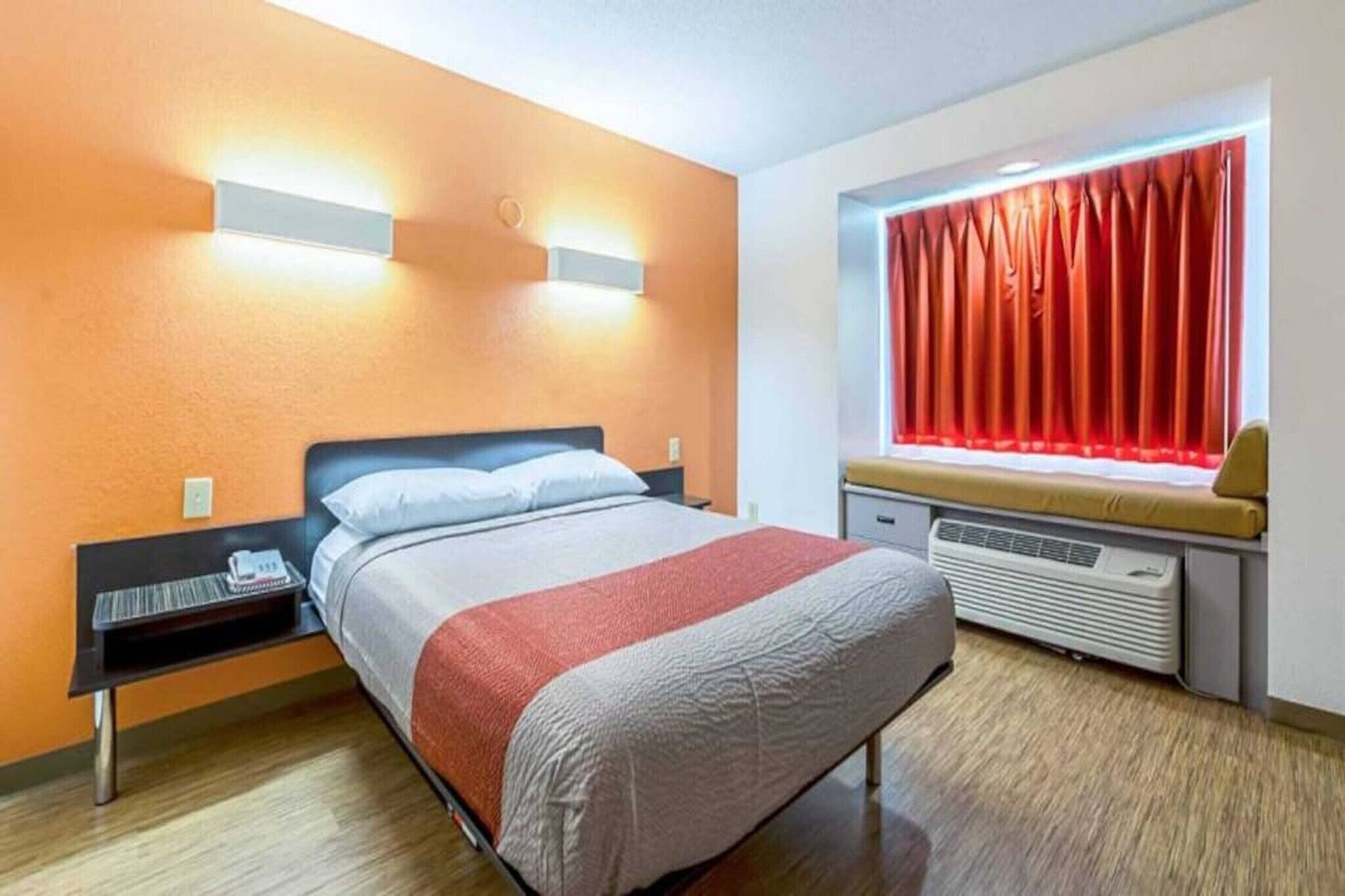 Ein Hotelzimmer mit Bett, Nachttisch und einem fenster mit Vorhängen.