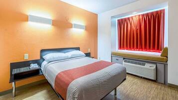 Ein Hotelzimmer mit Bett, Nachttisch und einem fenster mit Vorhängen.