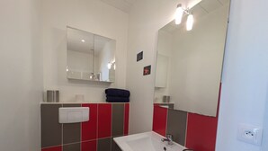 Casa de banho com uma pia branca, um espelho, uma sanita e azulejos vermelhos e cinzentos.