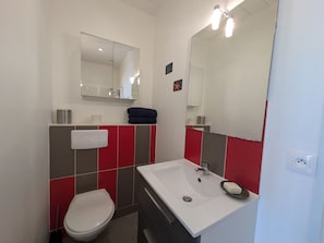Ein Badezimmer mit weißem Waschbecken, einem Spiegel, einer Toilette und roten und grauen Fliesen.