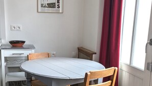 Uma sala de jantar com mesa redonda, cadeiras de madeira, um armário branco e uma cortina vermelha.