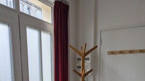 Um quarto com porta, cabideiro e janela com cortinas.