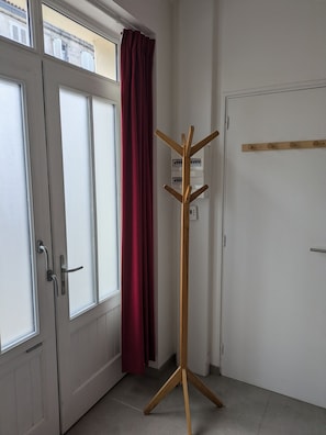 Ein Zimmer mit Tür, Kleiderhaken und einem mit Vorhängen versehenen Fenster.