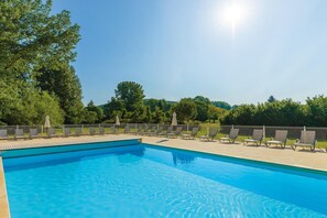 Une piscine d’un bleu éclatant, dotée de chaises longues et de parasols, et entourée d’une clôture et d’arbres.