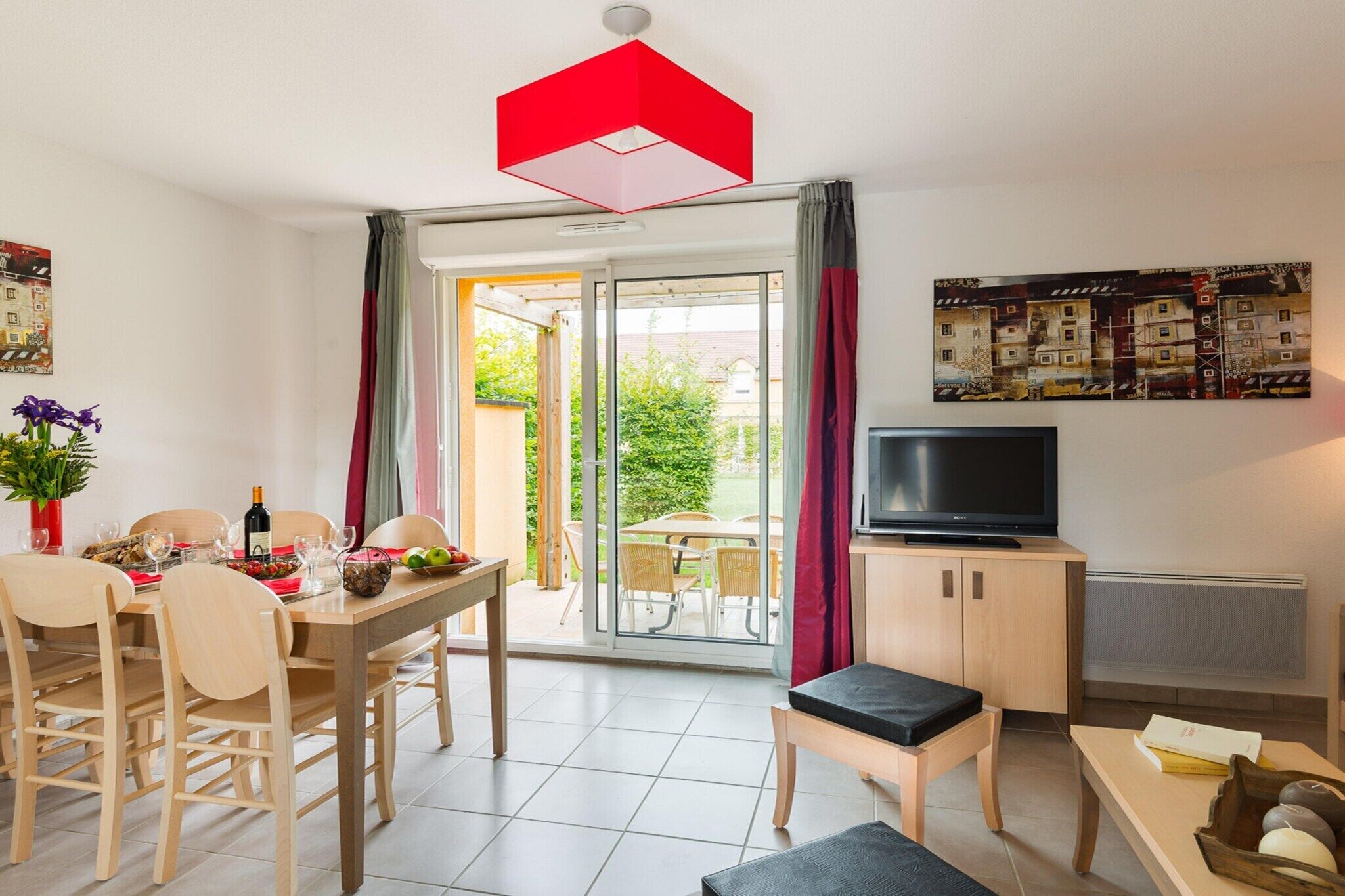 Una sala de estar moderna con comedor, televisor y puerta corrediza de vidrio que da a un espacio exterior.