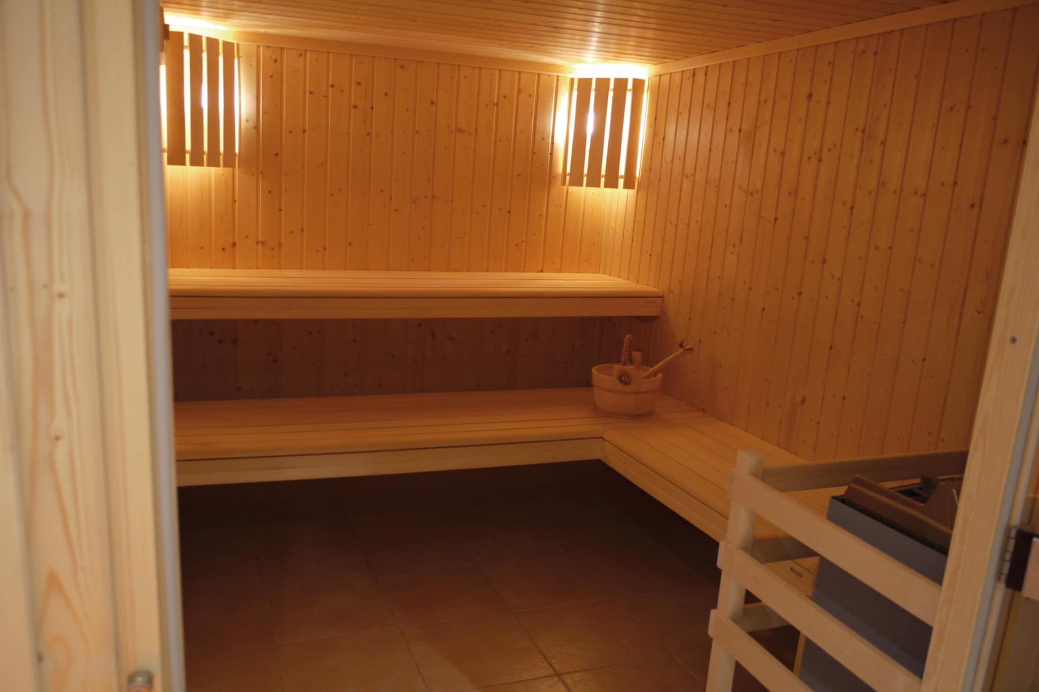 Et sauna-rum med træbænke og et bænk-sæde, et lille bord med en spand, og et trægelænder.