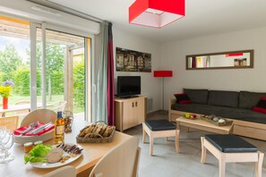 Ein modernes Wohnzimmer mit Sofa, Fernseher und Essbereich mit Tisch für zwei Personen.
