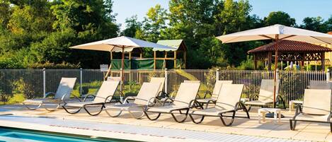 A poolside area with lounge chairs and umbrellas, surrounded by a fence and trees.