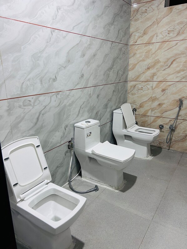 A bathroom with three toilets, a shower, and a marble wall.