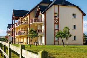 A multi-story building with balconies, a wooden fence, and a grassy lawn. - Stylish coastal apartment with shared pool (Fréhel)